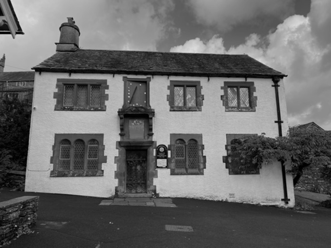 Greyscale photograph of Hawkshead Grammar School Building exterior, showing the wooden door and sandstone windows. 